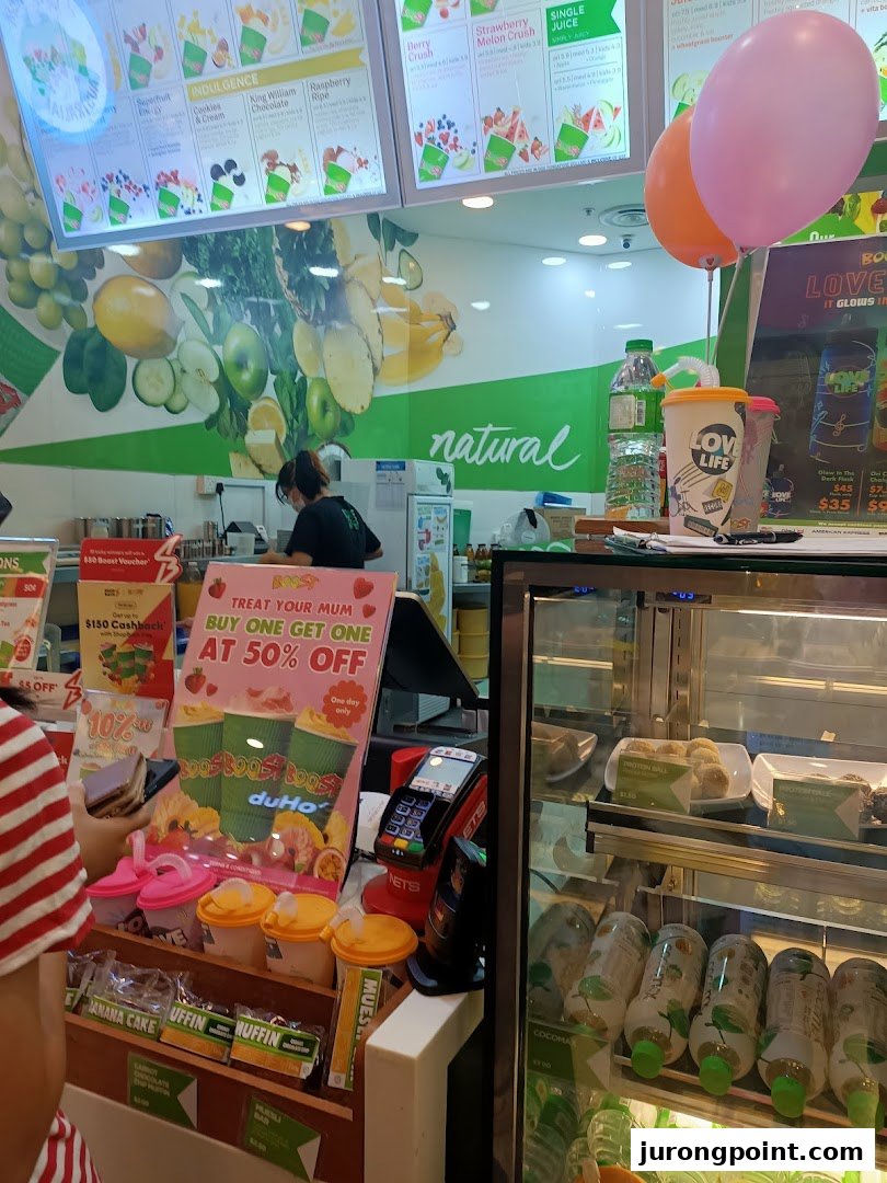 Interior view of a Boost Juice bar, showcasing menu boards, fresh produce, and a staff member.