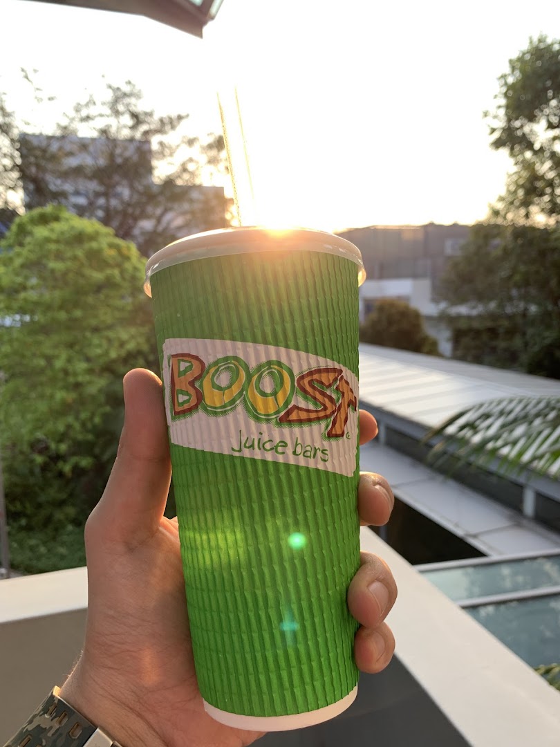 A hand holds a Boost Juice cup with a bright outdoor background, illuminated by sunlight.
