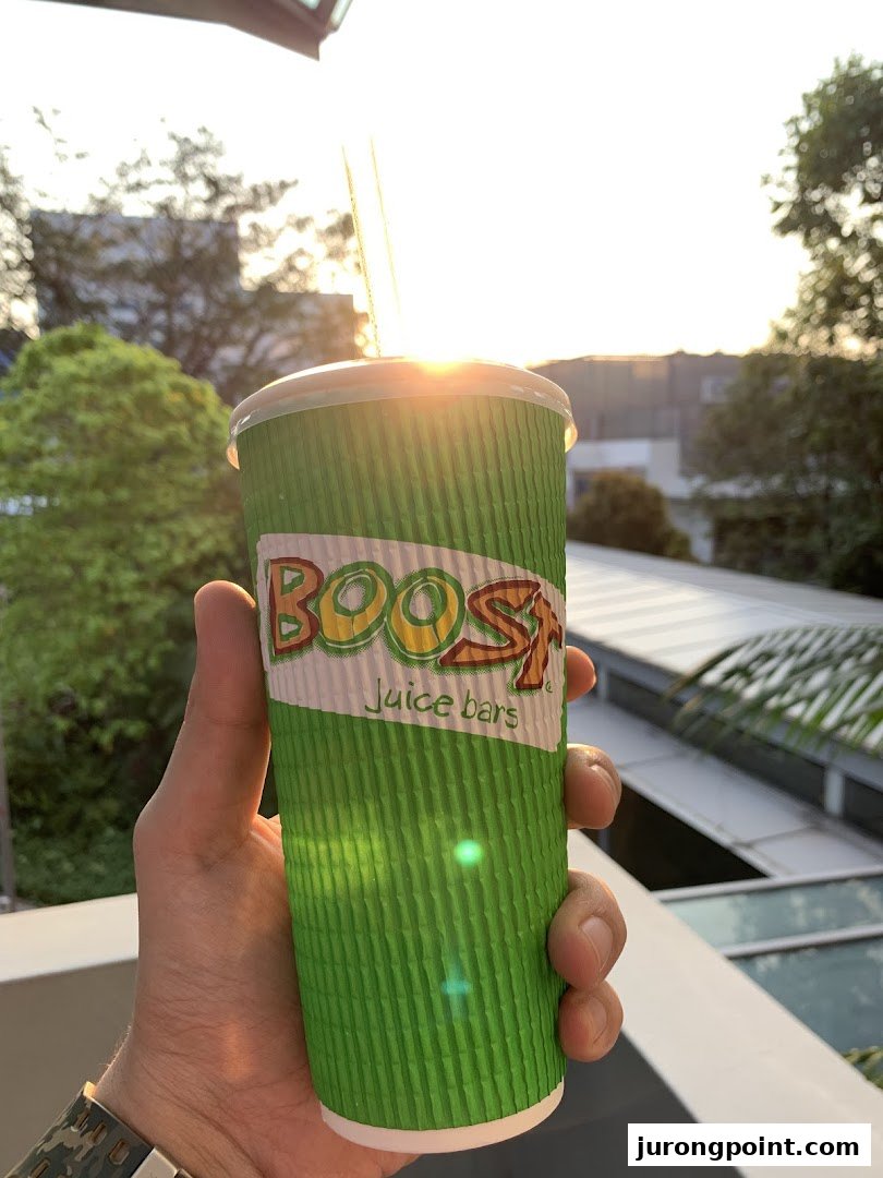 A hand holds a Boost Juice cup with a bright outdoor background, illuminated by sunlight.