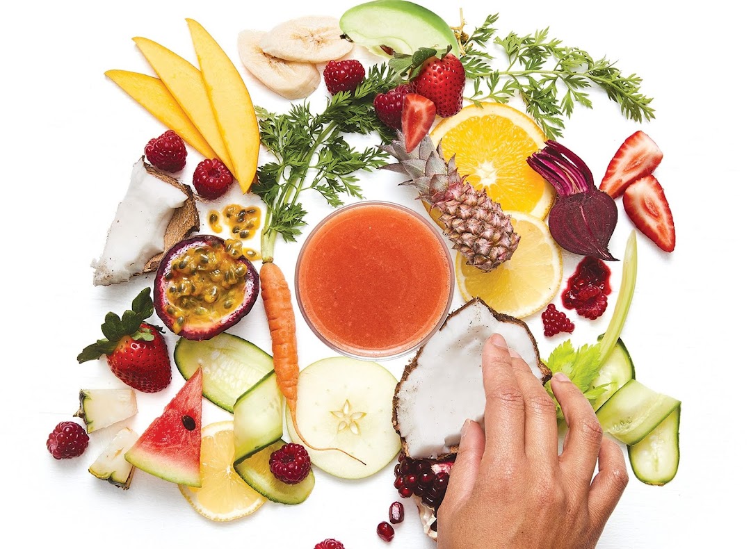A vibrant display of fresh fruits and vegetables surrounding a glass of juice, highlighting natural ingredients.
