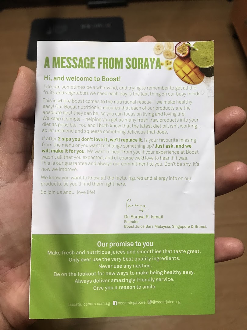A hand holds a welcome message and promise card from Boost Juice, featuring fruit imagery.