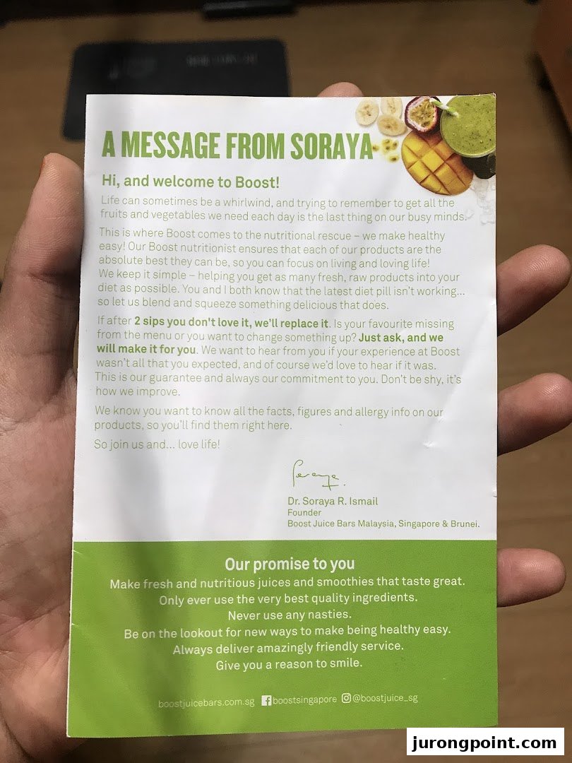 A hand holds a welcome message and promise card from Boost Juice, featuring fruit imagery.