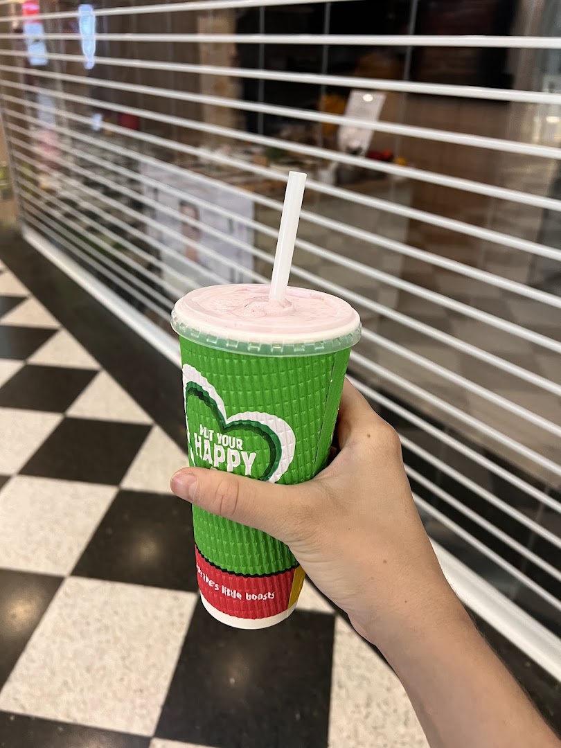 A hand holds a Boost Juice cup with a pink smoothie and straw, in front of a closed shop.