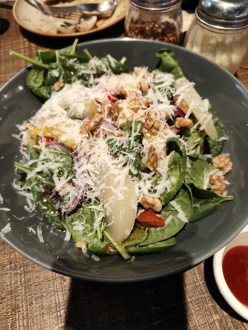 A vibrant salad with spinach, walnuts, pear, and grated cheese in a dark bowl on a wooden table.