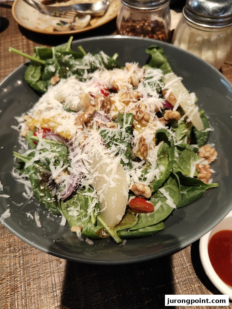 A vibrant salad with spinach, walnuts, pear, and grated cheese in a dark bowl on a wooden table.