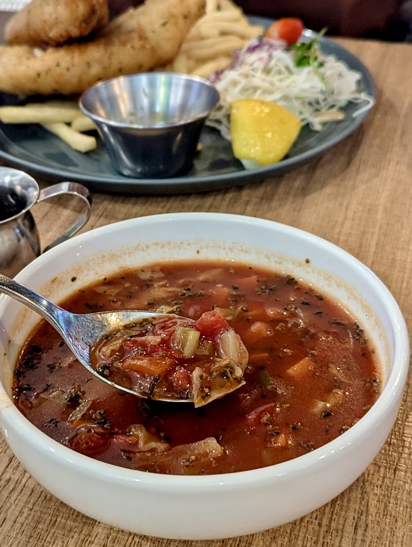 A close-up of a hearty vegetable soup with fish and chips in the background at Brio.