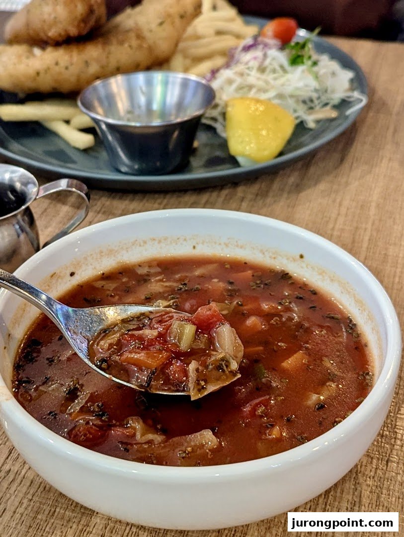 A close-up of a hearty vegetable soup with fish and chips in the background at Brio.