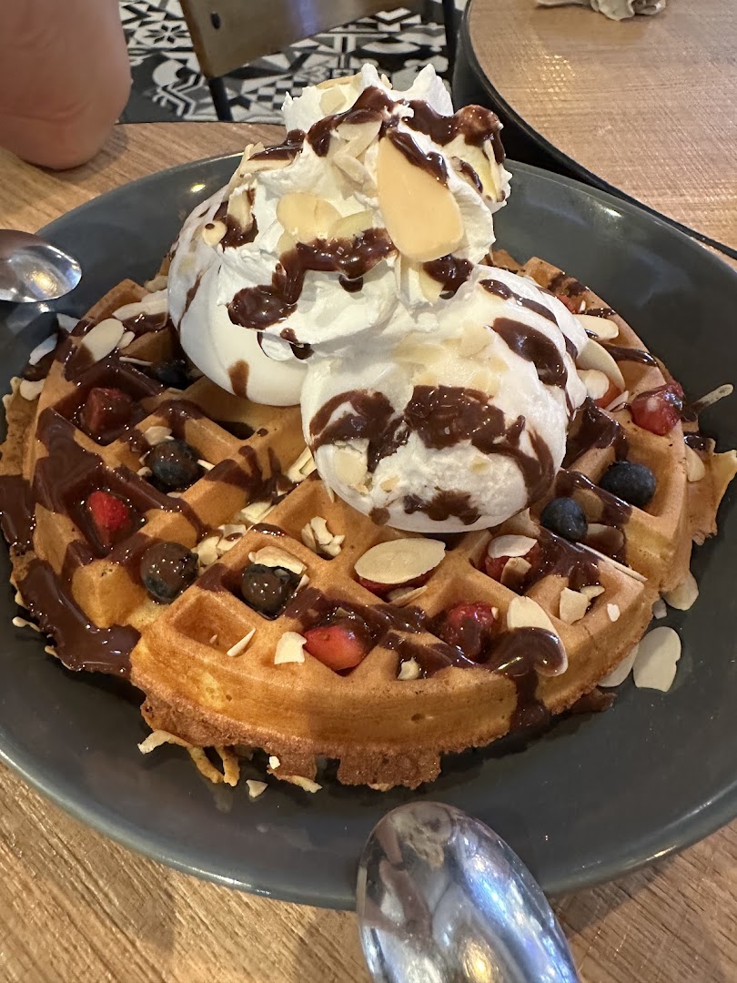 A delicious waffle topped with whipped cream, chocolate drizzle, fresh berries, and sliced almonds.
