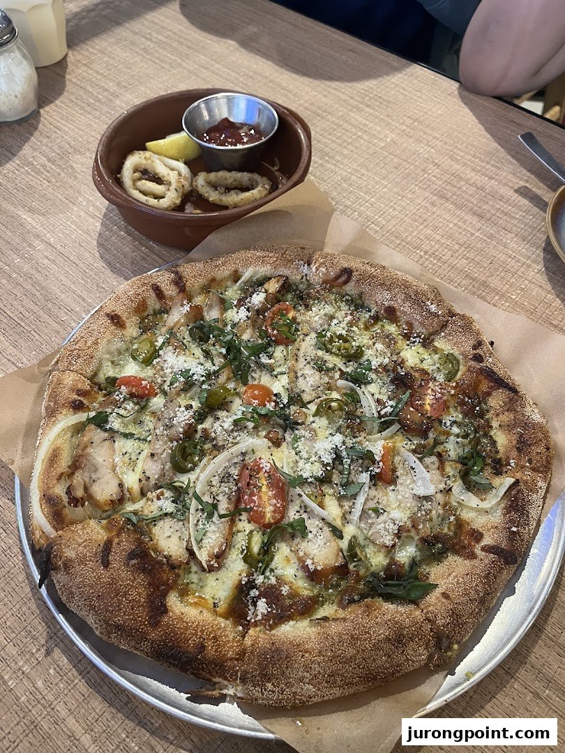 A gourmet pizza with chicken and vegetables, alongside crispy calamari, served on a rustic wooden table.