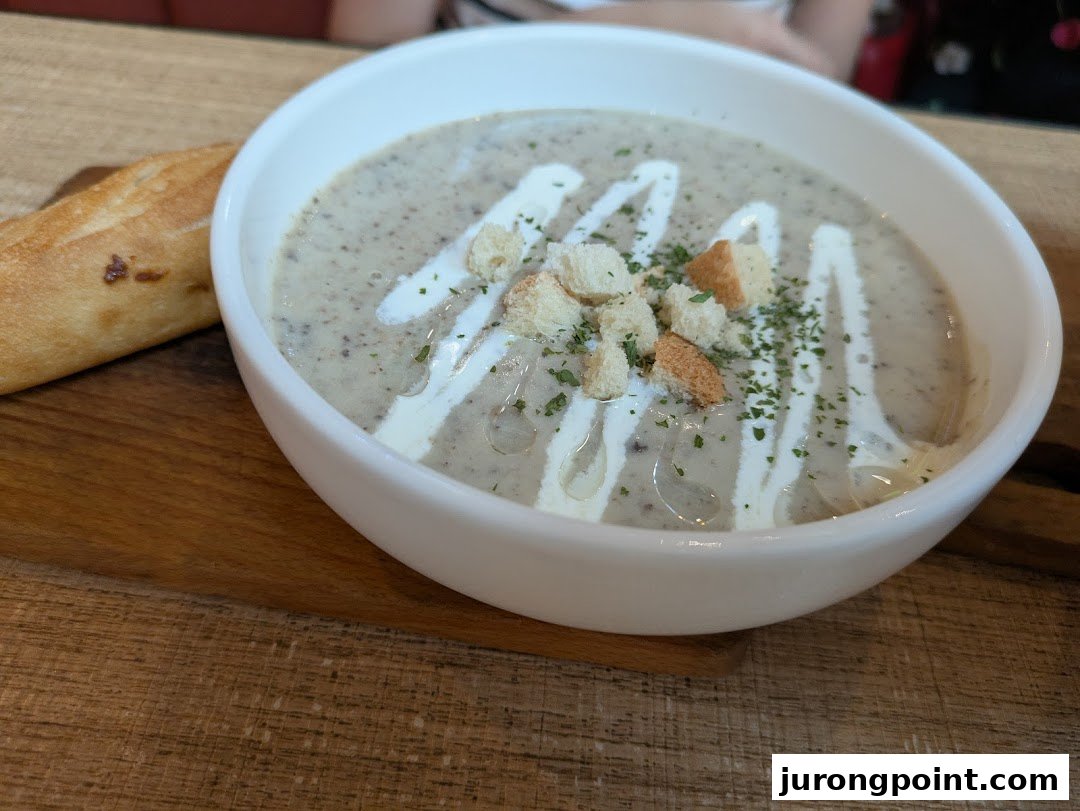 A creamy bowl of mushroom soup topped with croutons and herbs, served with a side of bread.