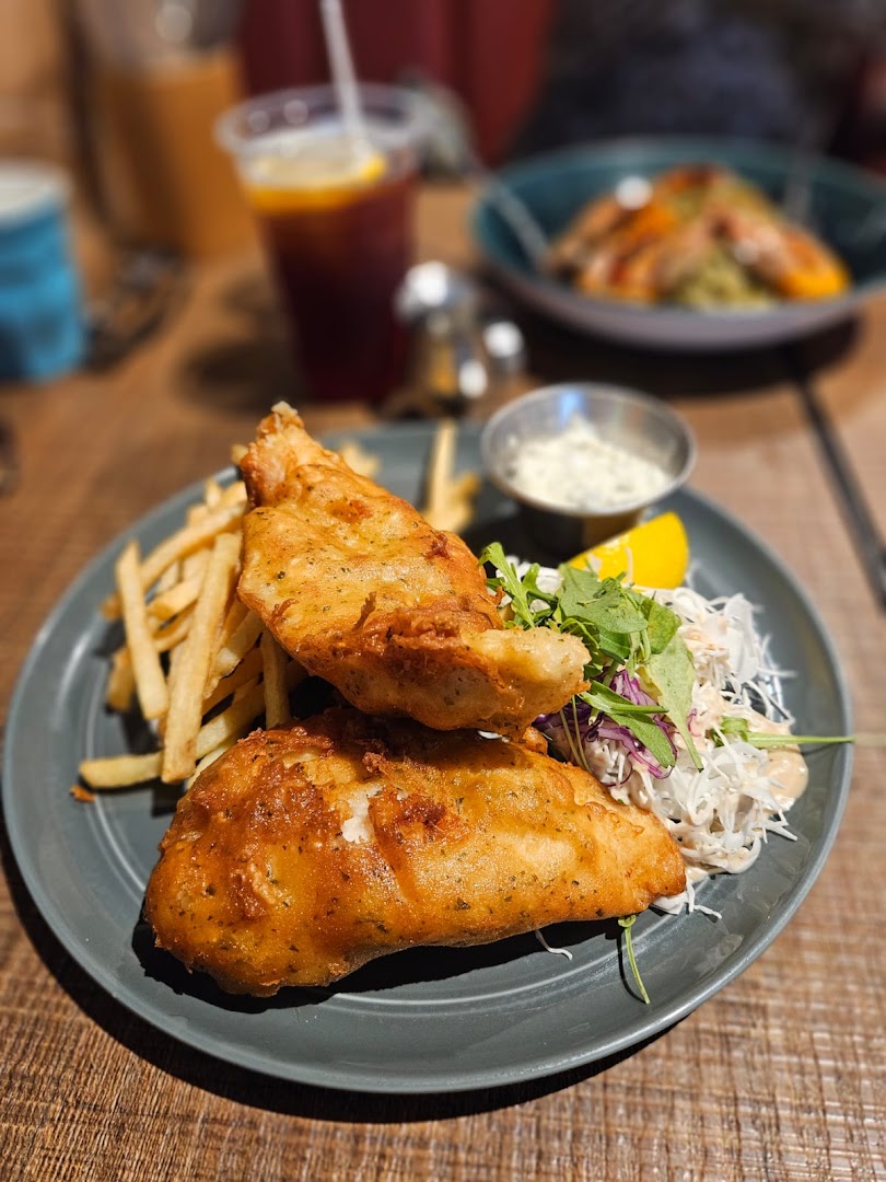 A plate of golden-fried fish and chips with coleslaw, tartar sauce, and a drink at Brio.