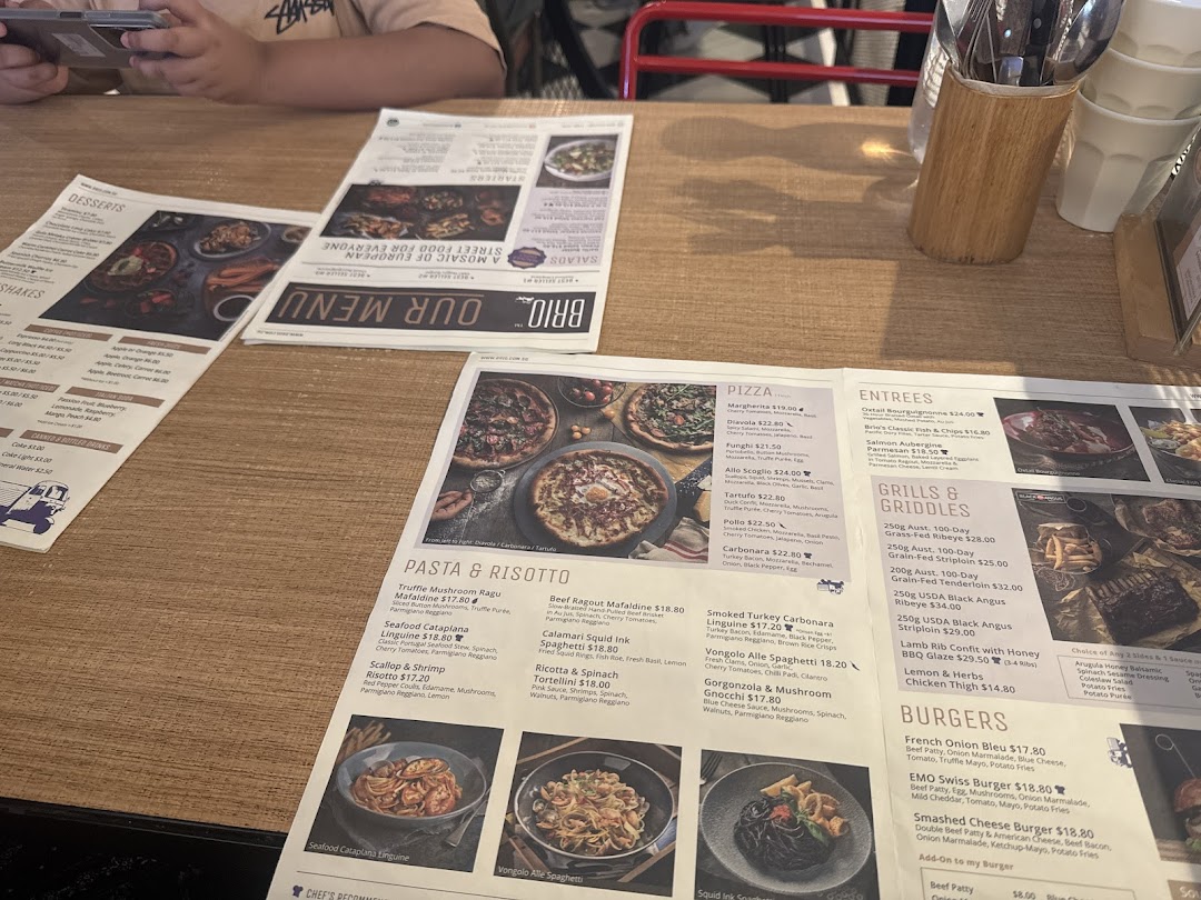 Multiple menus from Brio restaurant displayed on a wooden table, showing various food categories.