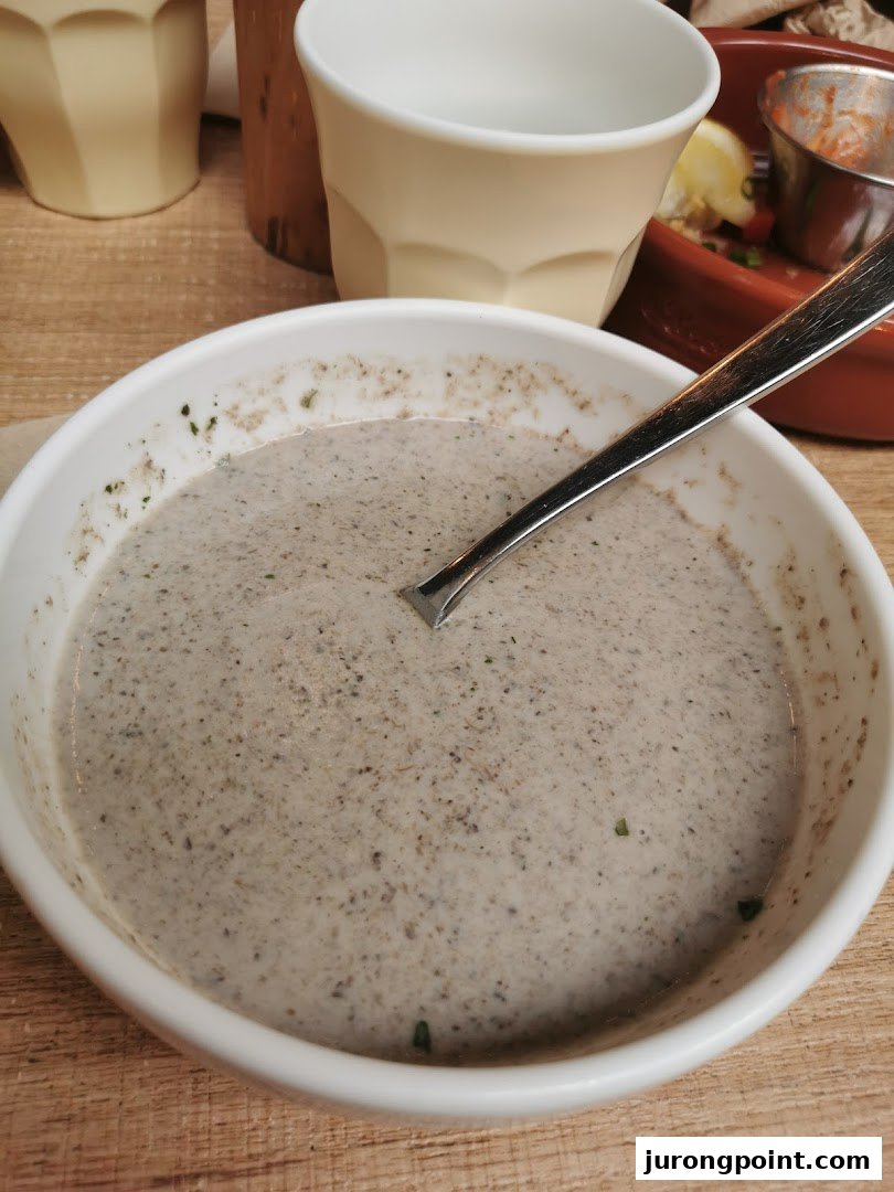 A close-up of a creamy, speckled soup in a white bowl with a spoon, on a wooden table.