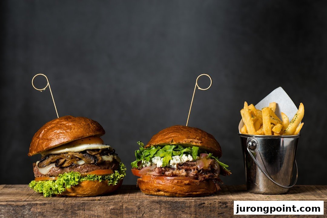 Two gourmet burgers with various toppings and a bucket of golden fries on a wooden surface.