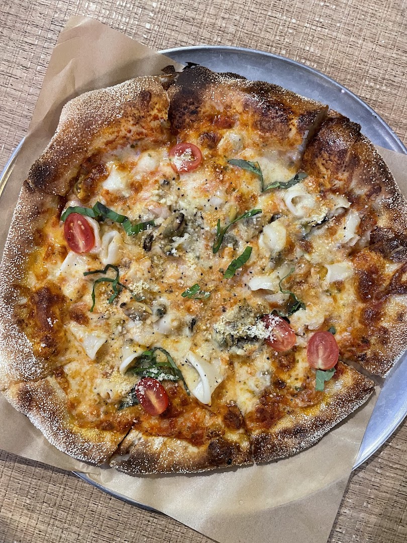 A close-up of a delicious seafood pizza with cherry tomatoes and fresh herbs on a metal tray.