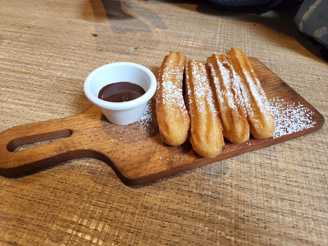 Five sugar-dusted churros and a ramekin of chocolate dipping sauce on a wooden board.