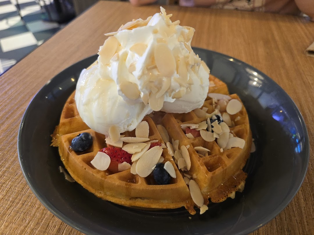 A delicious waffle topped with vanilla ice cream, whipped cream, berries, and sliced almonds.