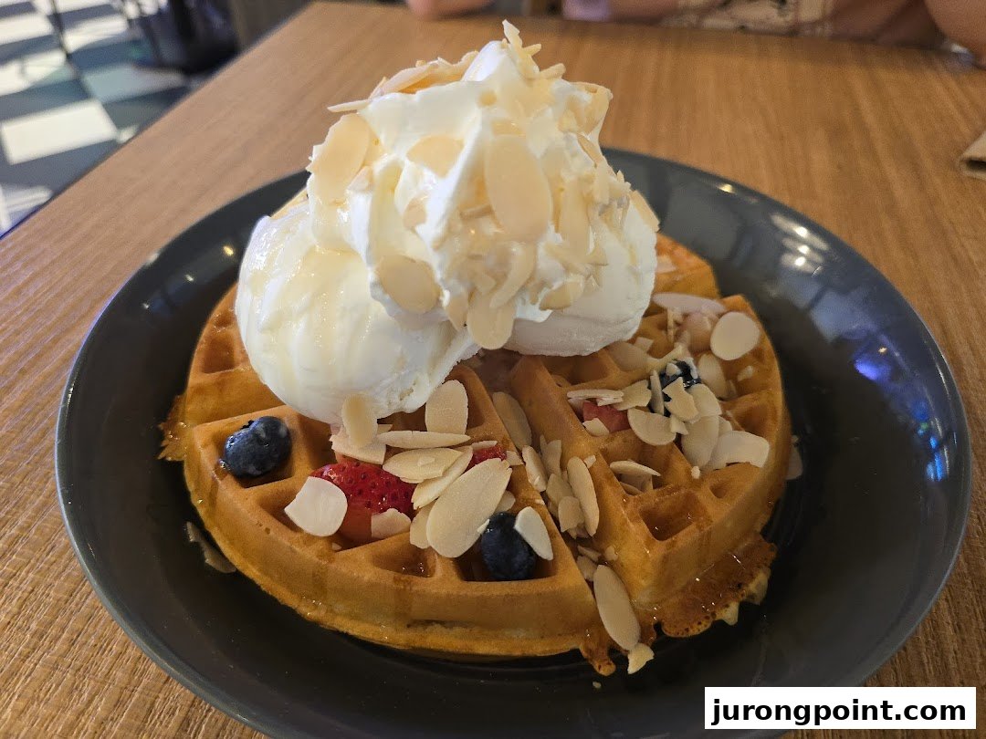 A delicious waffle topped with vanilla ice cream, whipped cream, berries, and sliced almonds.