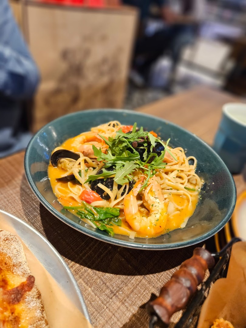 A vibrant bowl of seafood pasta with shrimp, mussels, and arugula on a wooden table.