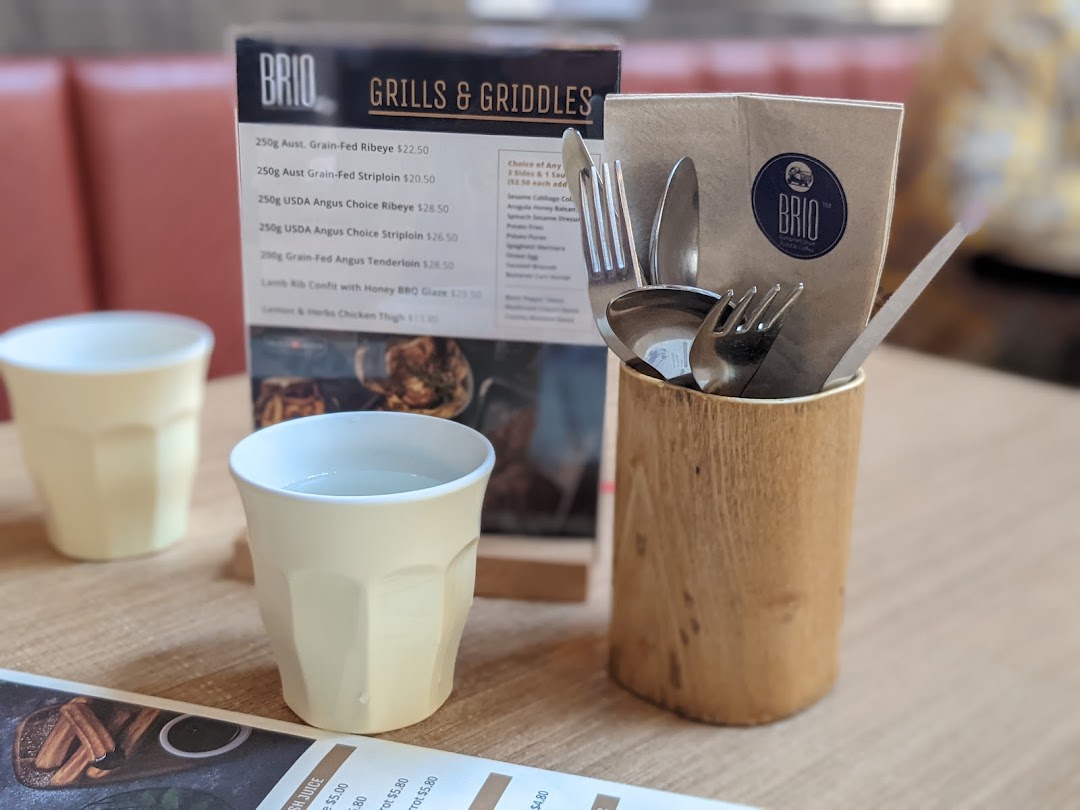 A table setting at Brio featuring a menu for grills and griddles, with cups and cutlery.