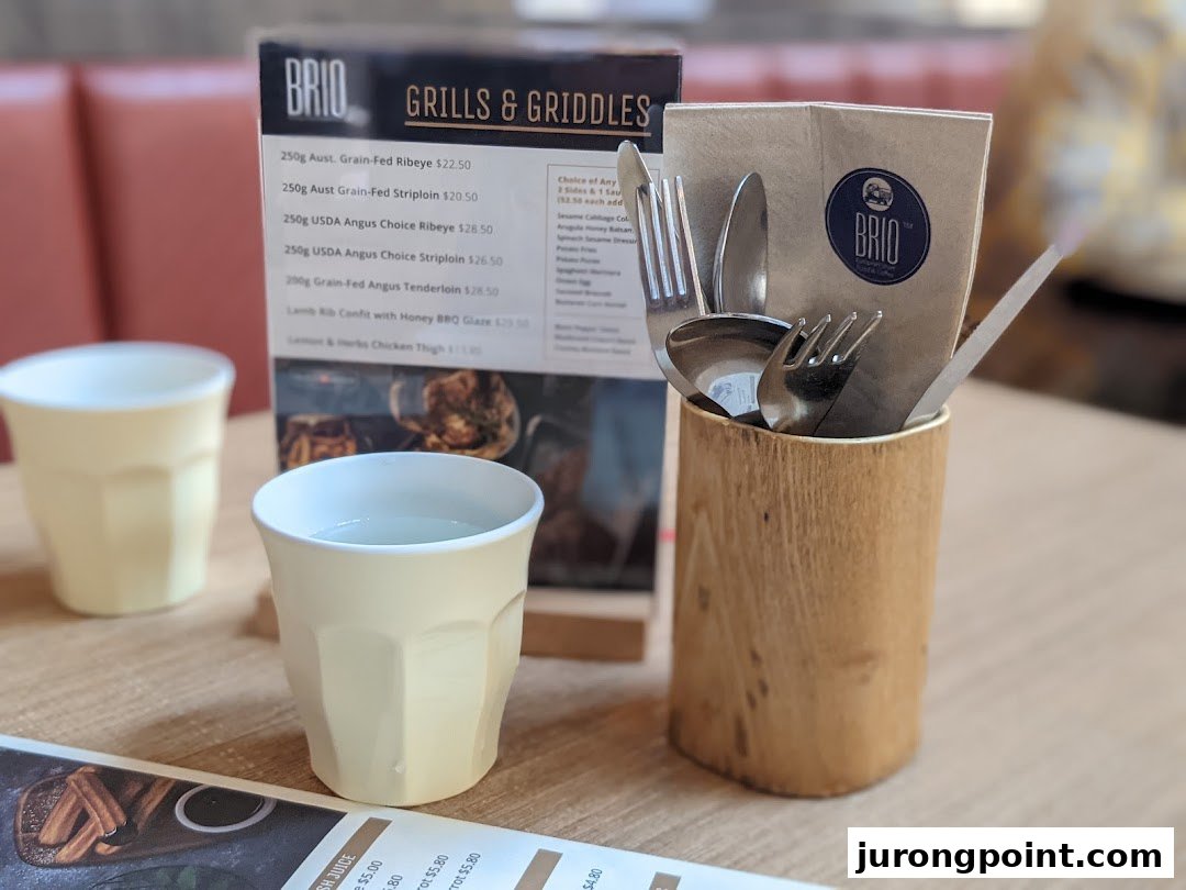A table setting at Brio featuring a menu for grills and griddles, with cups and cutlery.
