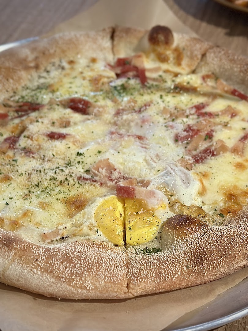 A close-up of a delicious pizza topped with creamy sauce, bacon, herbs, and a perfectly cooked egg yolk.