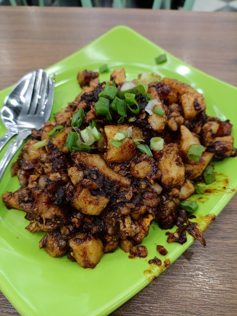 A vibrant green plate holds a delicious serving of stir-fried dark carrot cake, garnished with fresh spring onions.