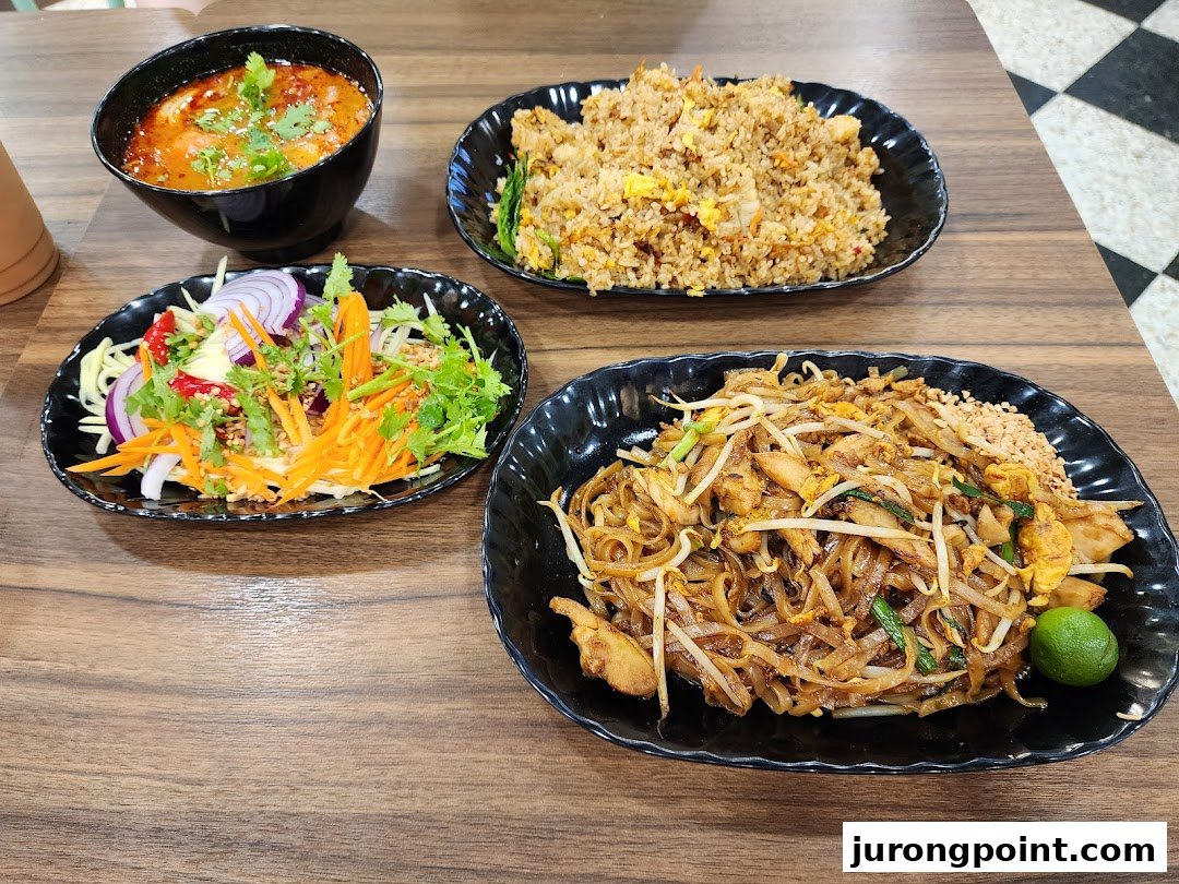 A table showcasing a variety of Asian dishes including Pad Thai, fried rice, a fresh salad, and a soup.