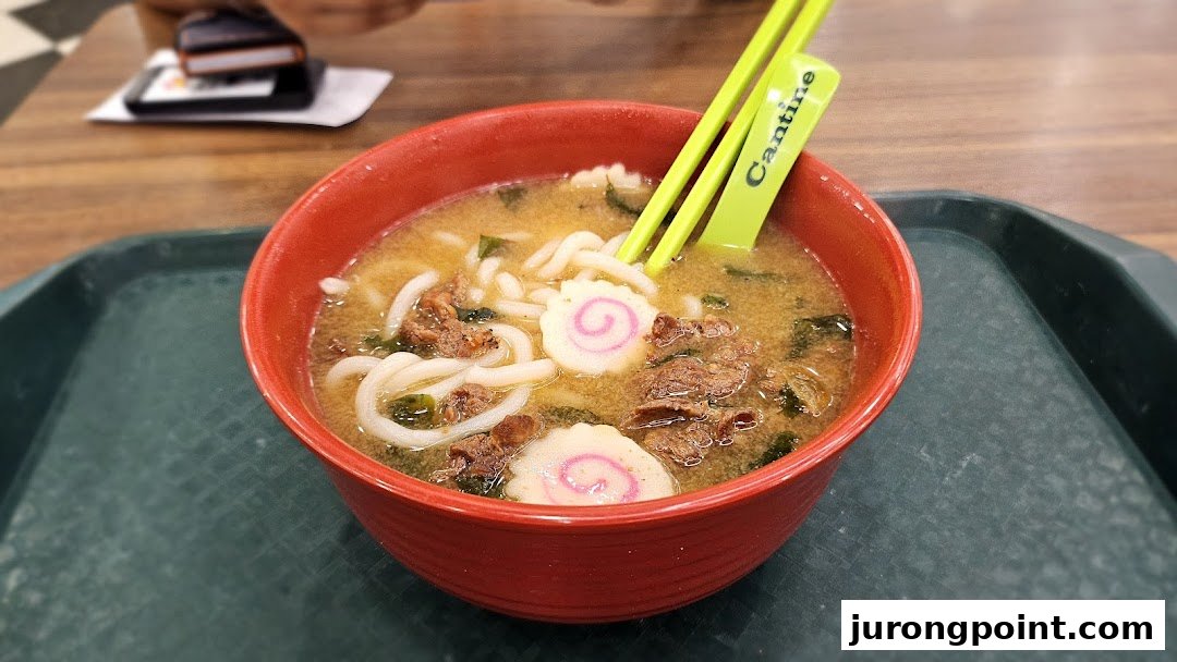 A vibrant red bowl of hot ramen or udon noodles with meat, seaweed, and fish cakes.
