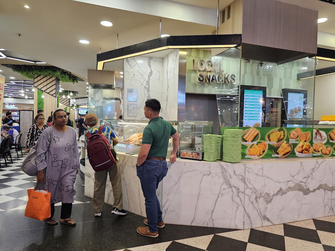 A bustling food stall counter featuring local snacks and a digital menu display within a mall.