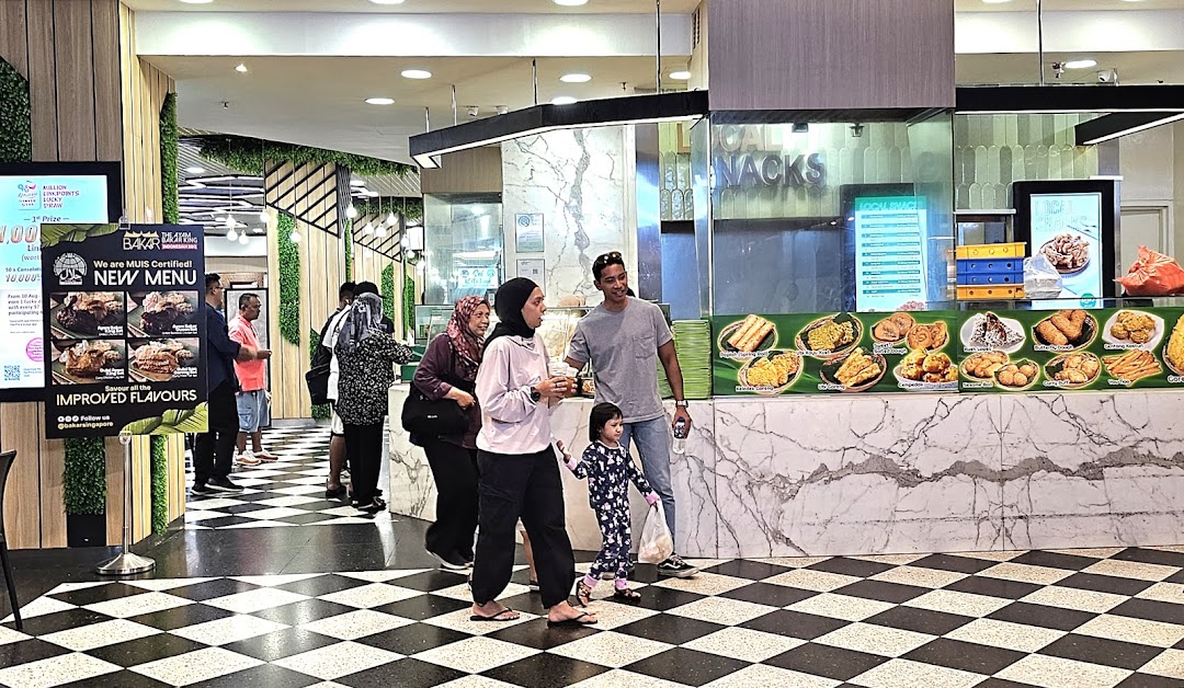 A vibrant scene at Cantine by Kopitiam, featuring a counter with various local snacks and customers.