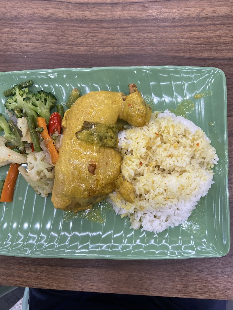 A plate of chicken curry with rice and mixed vegetables on a green rectangular plate.