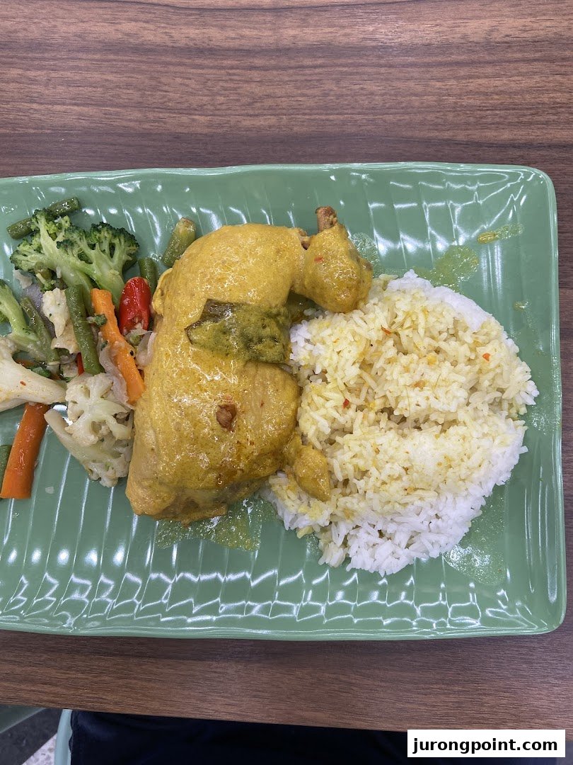 A plate of chicken curry with rice and mixed vegetables on a green rectangular plate.