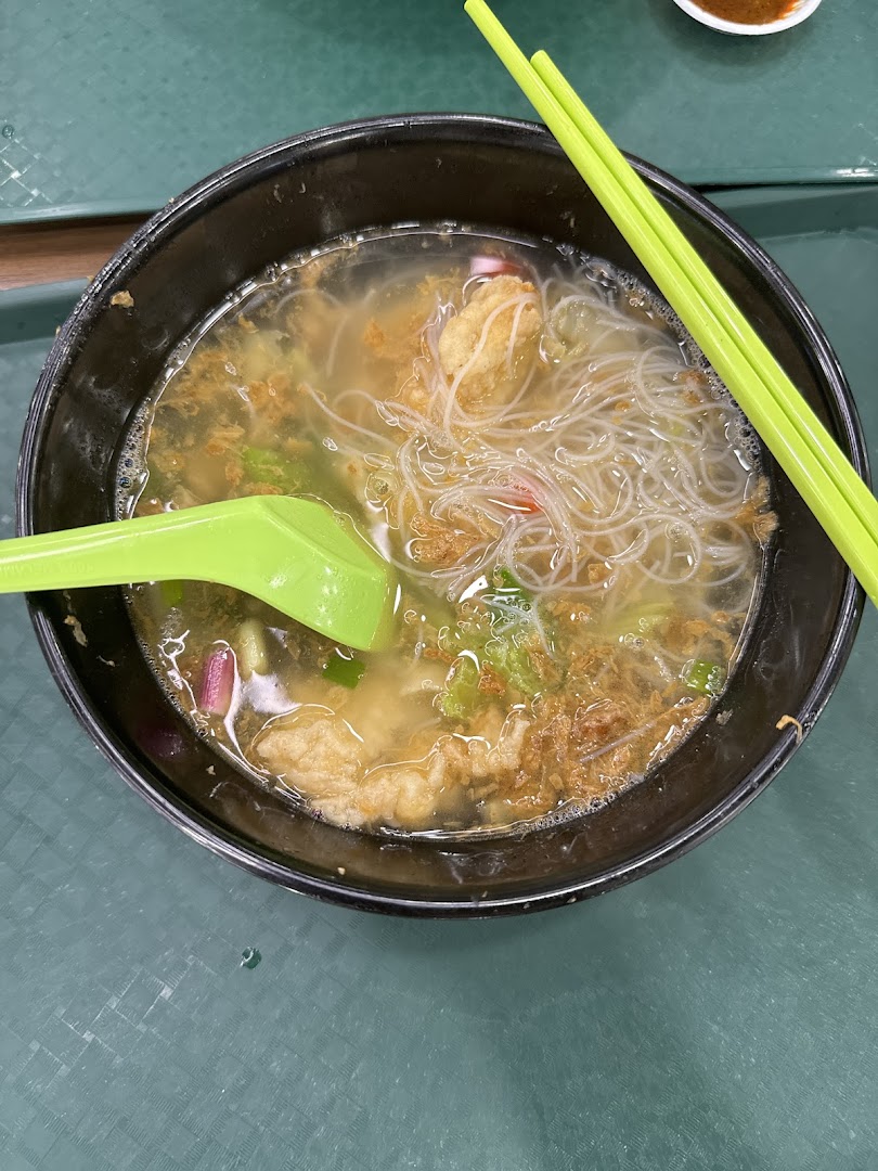 A close-up of a bowl of clear noodle soup with various ingredients and green chopsticks.