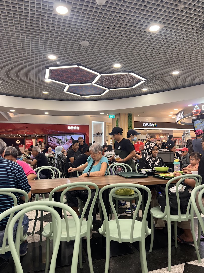 Diners enjoying meals at communal tables in a bustling food court setting with modern lighting.