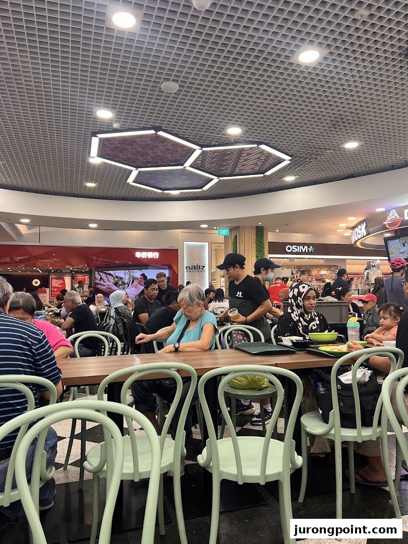 Diners enjoying meals at communal tables in a bustling food court setting with modern lighting.
