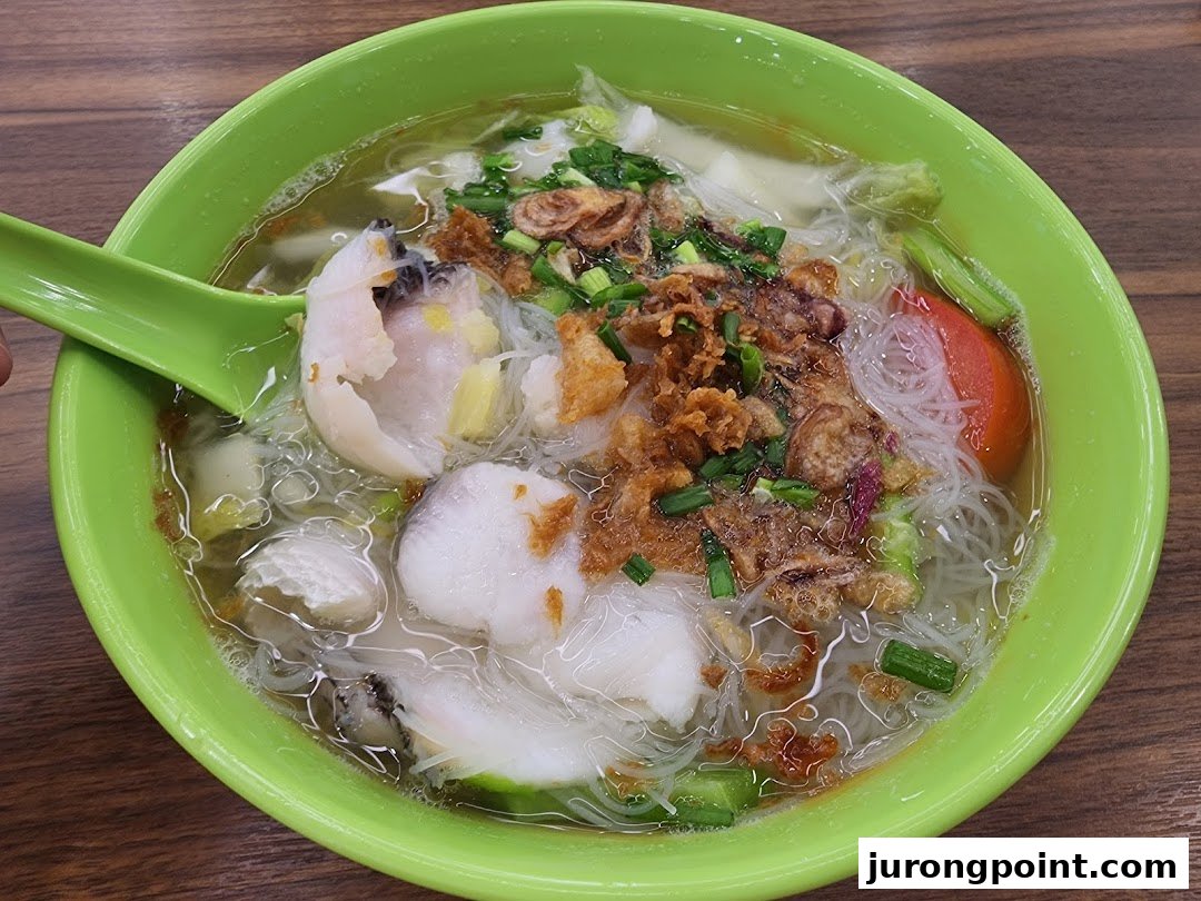 A vibrant bowl of fish bee hoon soup with tender fish slices, fried shallots, and vegetables.