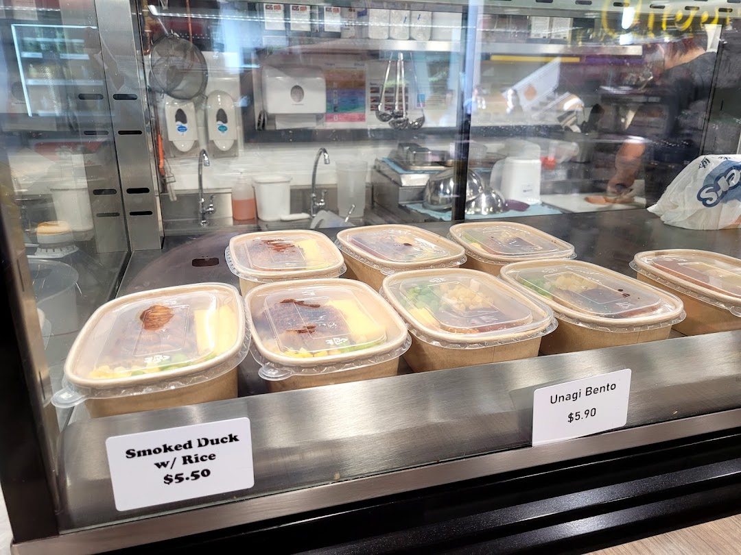 Pre-packaged meals like Smoked Duck with Rice and Unagi Bento displayed with prices in a glass case.