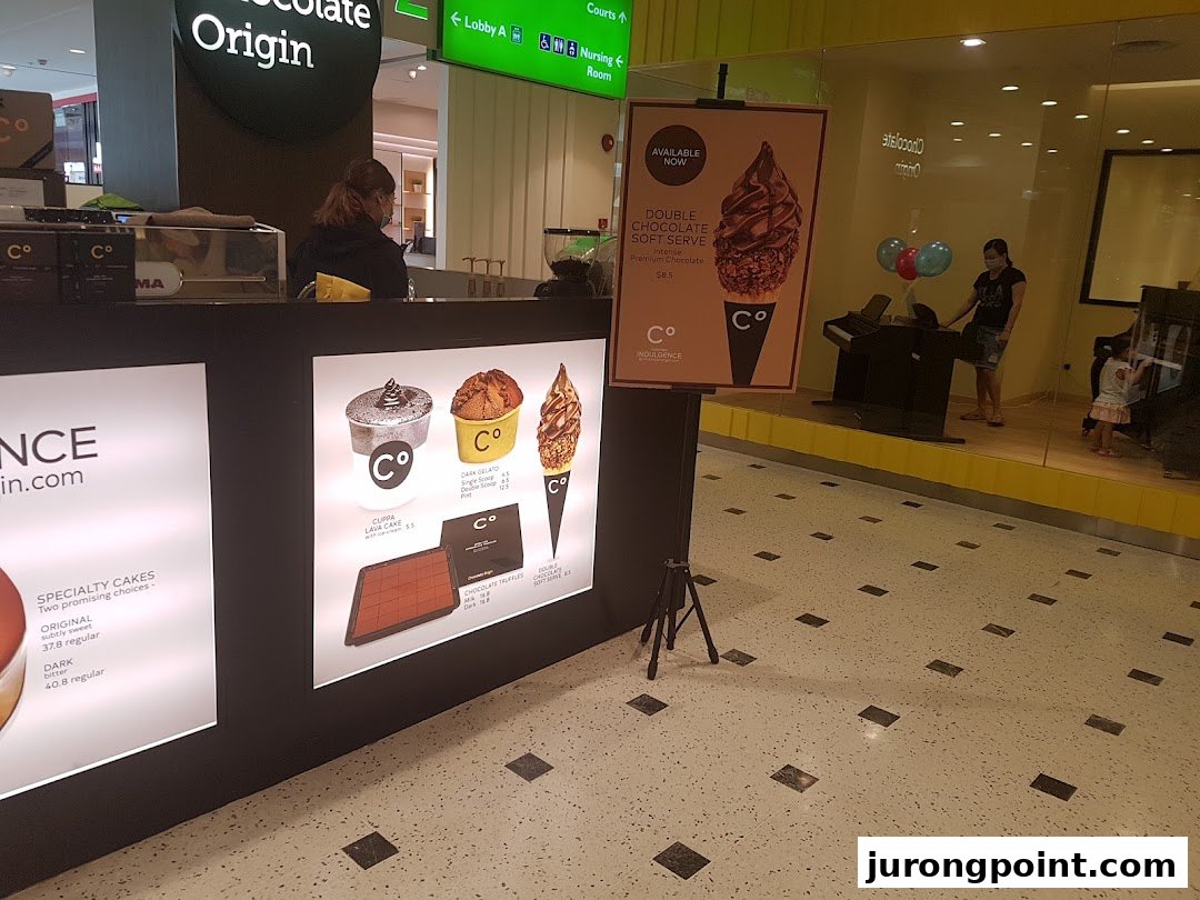 An interior view of Chocolate Origin, showcasing their counter, staff, and tempting chocolate desserts and soft serve displays.