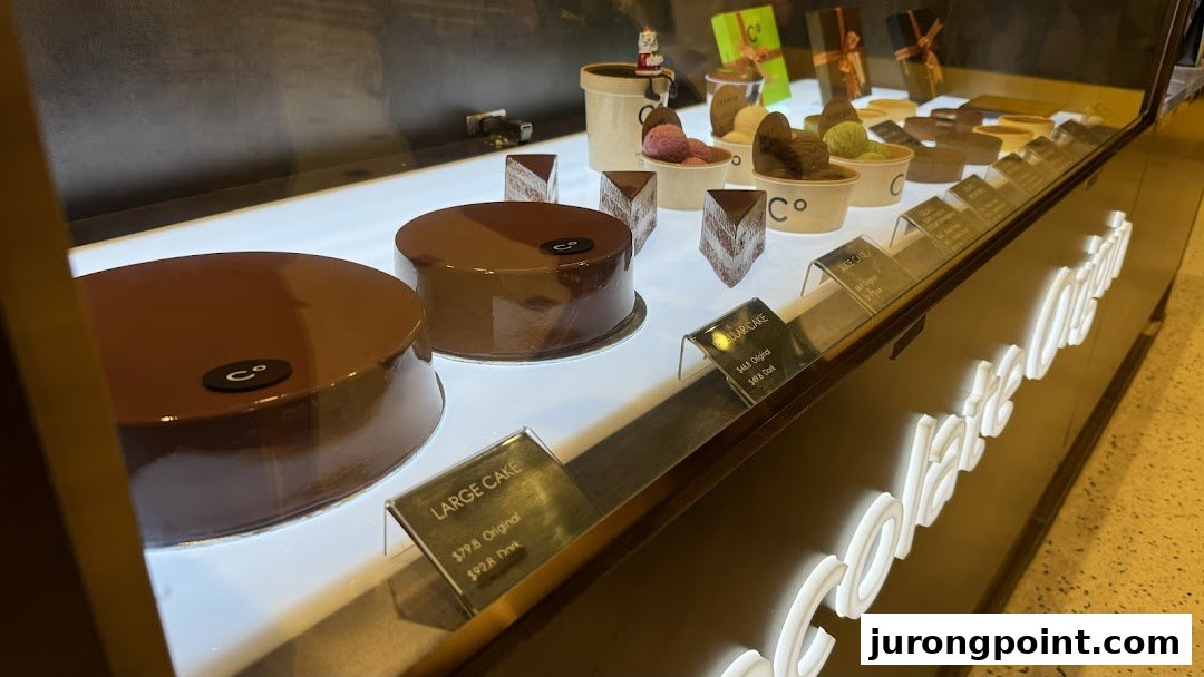 A brightly lit display case showcasing Chocolate Origin's signature chocolate cakes and desserts.