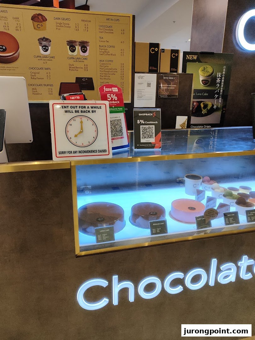 A Chocolate Origin counter featuring a menu board, cake display, and payment options.