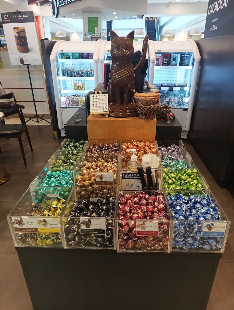 A vibrant display of assorted chocolates, featuring a large chocolate cat statue and various flavors like dark, strawberry, and salted milk.