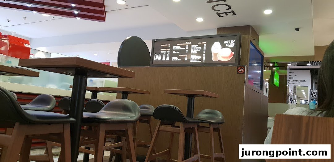 Interior view of Chocolate Origin cafe with high tables, stools, and a digital menu board displaying offerings.