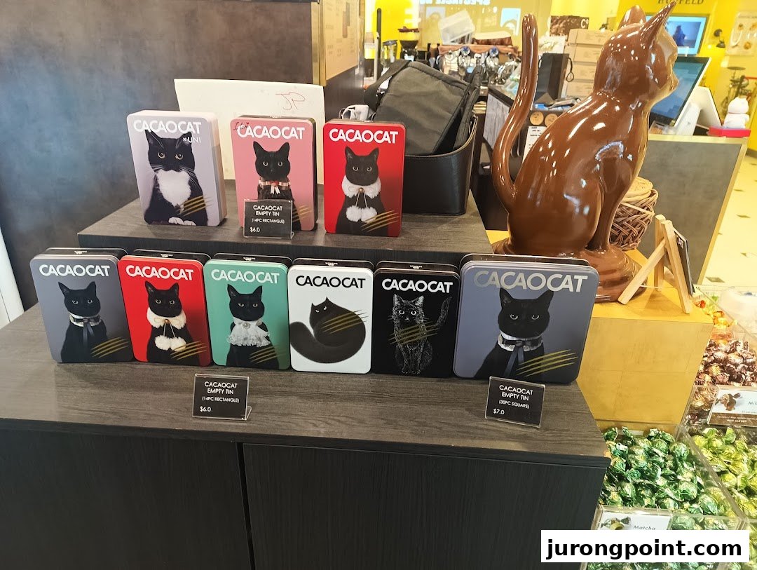 A display of CACAOCAT chocolate tins featuring various cat designs, alongside a large chocolate cat statue.