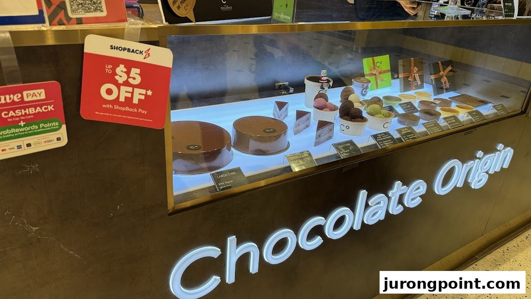 A brightly lit display case at Chocolate Origin showcasing various chocolate cakes, ice cream, and desserts.