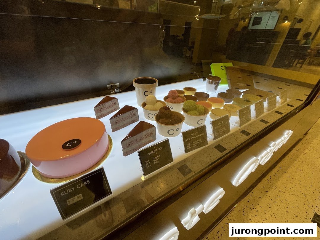 A vibrant display case showcasing a variety of decadent cakes and creamy gelato flavors at Chocolate Origin.