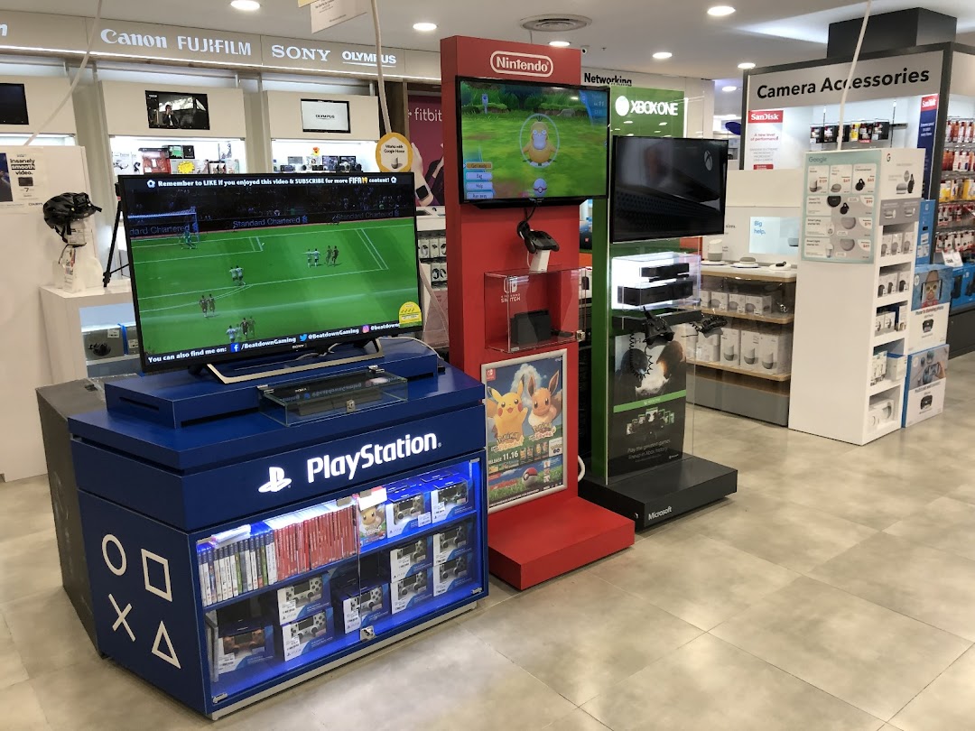 An electronics store interior showcasing gaming consoles, cameras, and accessories from brands like PlayStation, Nintendo, and Xbox.