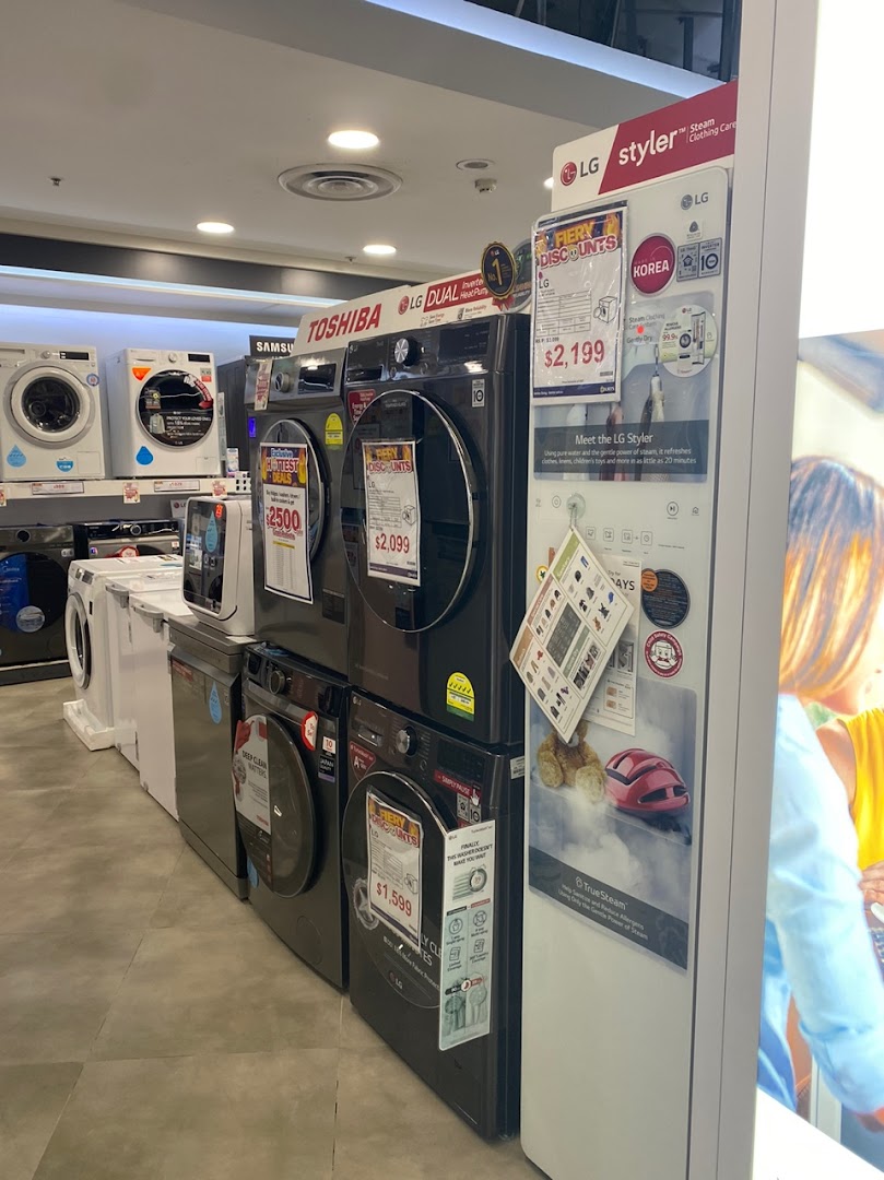 An electronics store aisle showcasing various washing machines and an LG Styler appliance.
