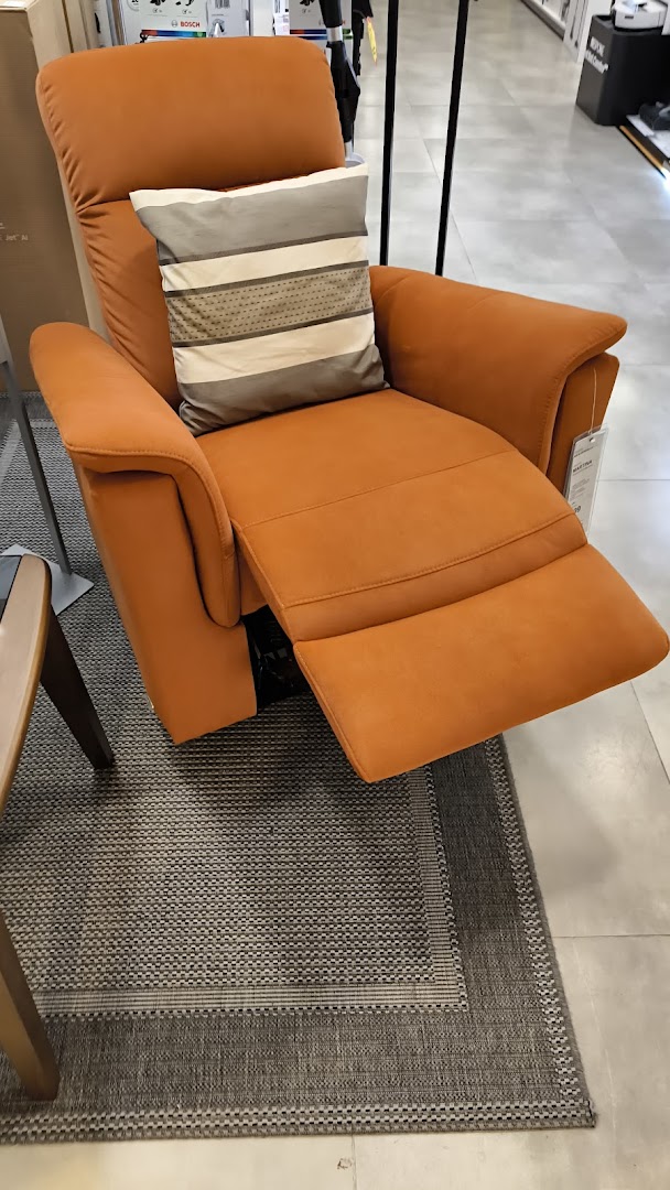 An orange recliner chair with a striped pillow sits on a patterned rug inside a retail store.