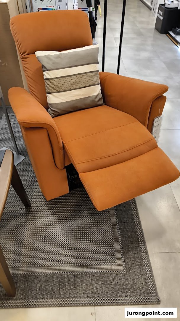 An orange recliner chair with a striped pillow sits on a patterned rug inside a retail store.
